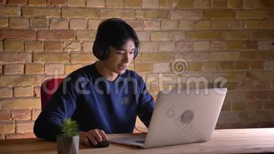 一位年轻的韩国商人戴着耳机在室内笔记本电脑上打视频电话的特写照片